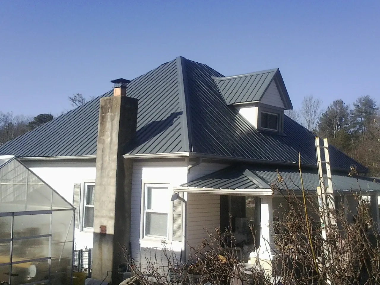 Dark blue standing seam metal roof on a white farmhouse with dormer — Slate & Tile Roof Repair by Roofing Brothers in Oldhams