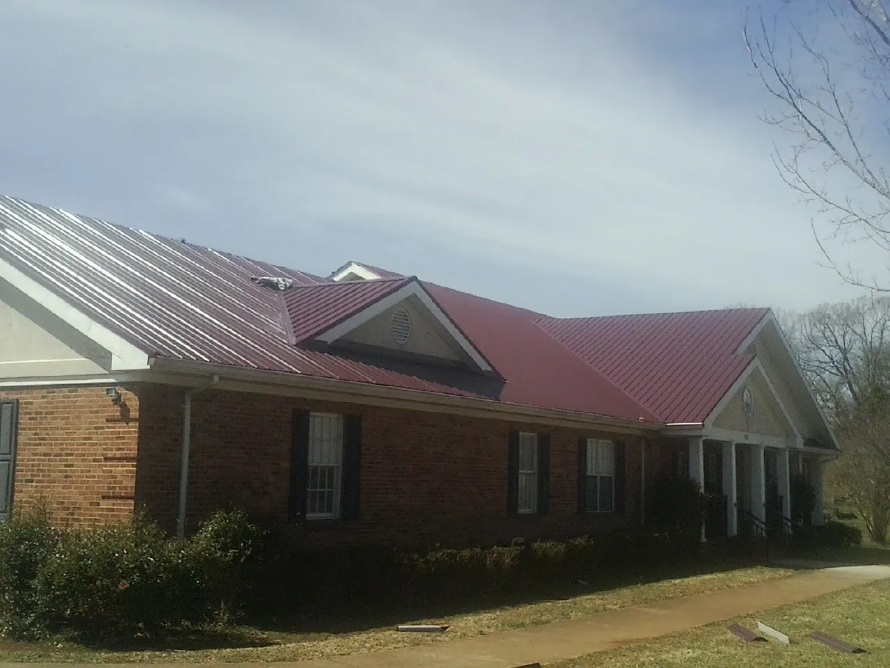 Red metal roof with gabled entries on a long brick building, from a Hail Damage Roof Repair job in Oldhams