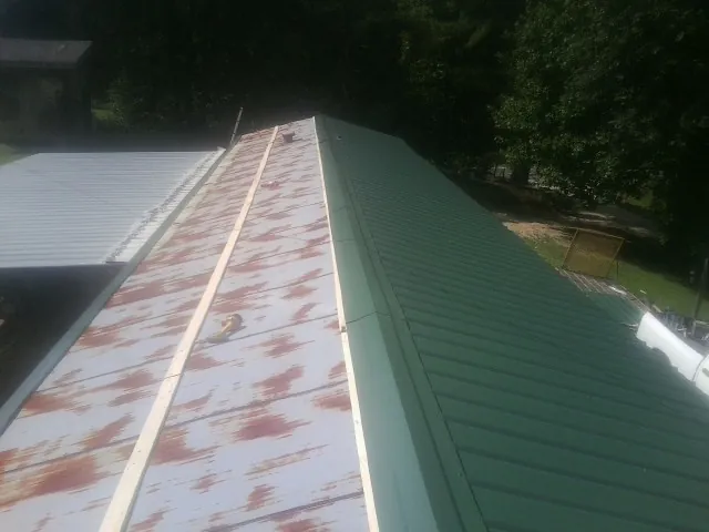 Old rusted panels beside newly installed green metal roofing — Wind Damage Roof Repair by Roofing Brothers in Oldhams