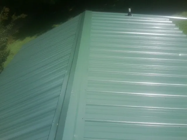 New green metal panels meeting at the ridge of a roof — Flat Roof Repair work by our crew in Oldhams