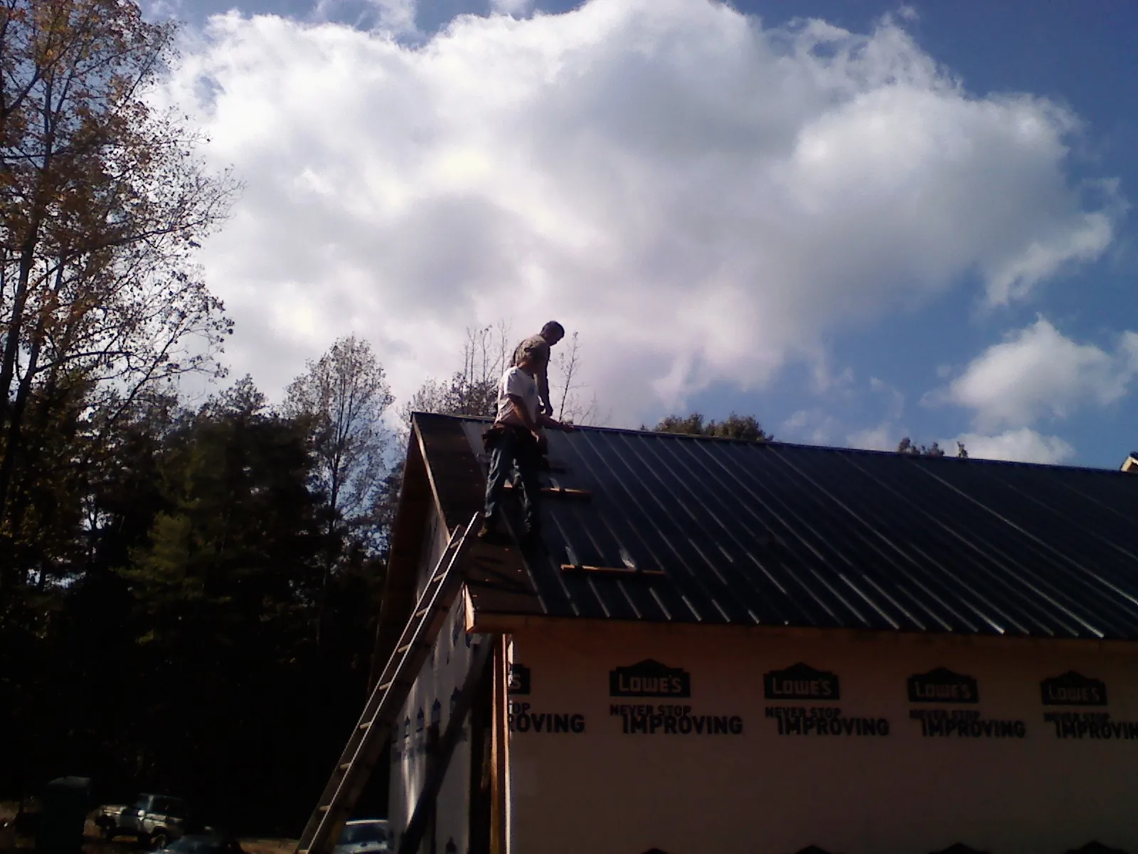 Roofer fastening dark metal panels high against a cloudy sky, from a Roof Inspection job in Oldhams