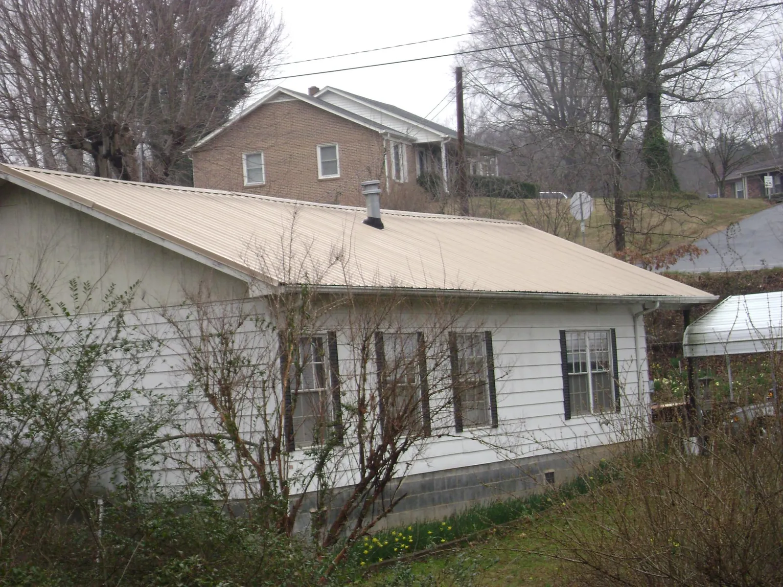 Tan metal roof on a white sided house set into a hillside — Commercial Roofing by Roofing Brothers in Oldhams